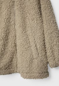 Beige, textured fleece jacket with a curly surface. Features a front zipper and side pockets, offering a cozy appearance and warmth.