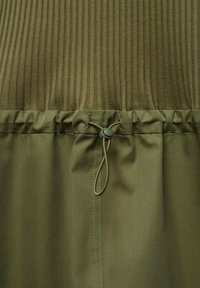 Olivově zelený oděv s žebrovanou texturou v horní části a hladkým materiálem s nastavitelnou šňůrkou v pase.