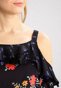 Schwarzes Off-Shoulder-Top mit rüschendetails, floralem Muster in Lila, Rot und Gelb sowie einem leichten, strukturierten Stoff.