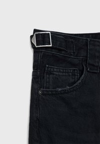 Primo piano di jeans in denim nero che mostra una tasca frontale, un passante per cintura e una fibbia regolabile in argento sulla vita.