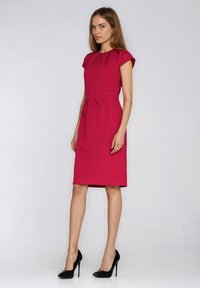 Dopasowana karmazynowa sukienka z krótkimi rękawkami typu cap, ze zakładkami przy dekolcie i w talii, do kolan, w połączeniu z czarnymi szpilkami.