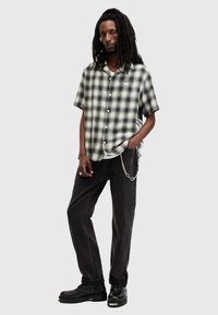 Chemise à manches courtes à carreaux noir et blanc avec fermeture à boutons sur le devant, portée avec un jean noir et des bottes noires présentant des détails en chaîne.