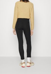 Pantalon noir ajusté avec une texture lisse, associé à un pull beige et des baskets sportives au design multicolore avec des accents rouges.