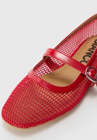 Červené topánky Mary Jane s prepracovanou sieťovinou a lesklým patentným pásikom. Špicatá špička a plochá podrážka pre pohodlie. Pracka ako akcent pre bezpečné uchytenie.