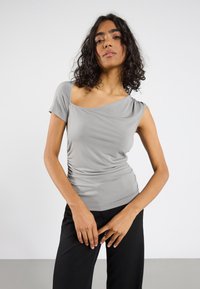 Ljusgrå, t-shirt med rund halsringning och korta ärmar, med draperad design och samlade sidodetaljer, i kombination med svarta byxor. Slät, stretchig tyg.