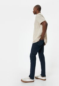 Beige neulepaita, tummansiniset farkut ja valkoiset tennarit ruskeilla yksityiskohdilla. Slim fit, pyöreä pääntie, lyhyet hihat ja hillitty rakenne.