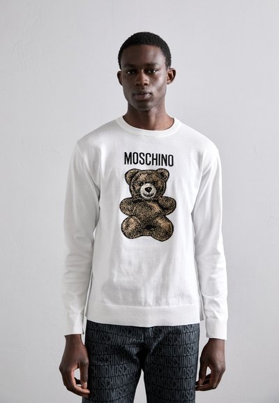 Tricou alb cu mânecă lungă, având un grafic texturat cu un urs și letteringul "MOSCHINO" deasupra. Asortat cu pantaloni negri, care prezintă un model repetitiv cu logo.