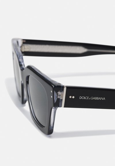 Black square sunglasses with dark lenses, clear temple accents, and silver hardware detailing featuring "Dolce & Gabbana" branding.
