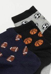 Trois paires de chaussettes en coton : bleu marine avec des motifs de football, noir avec des motifs de basket-ball, et gris avec des motifs de ballon de soccer.