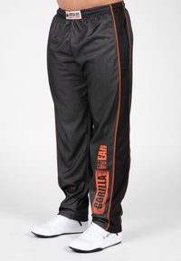 Zwarte sportieve broek met oranje zijstrepen en "GORILLA WEAR" verticaal gedrukt. Gemaakt van lichtgewicht stof en voorzien van een elastische tailleband.