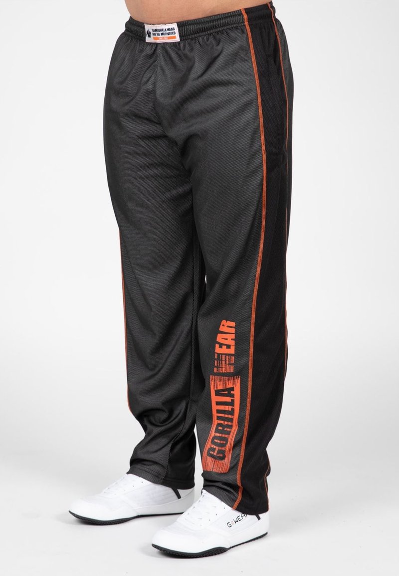 Zwarte sportieve broek met oranje zijstrepen en "GORILLA WEAR" verticaal gedrukt. Gemaakt van lichtgewicht stof en voorzien van een elastische tailleband.