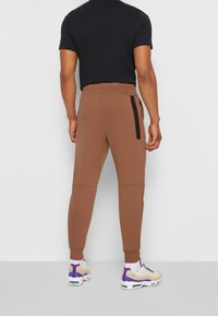 Bruna sweatpants med smal passform, har en sida med dragkedja, elastisk midja och ribbade muddar, kombinerat med färgglada sportskor.