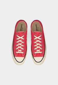 Κόκκινα πάνινα παπούτσια με λευκές τρύπες για τα κορδόνια και μπεζ κορδόνια. Διαθέτουν μπεζ προστατευτική μύτη και μαύρη ελαστική σόλα με αντίθετη ραφή.