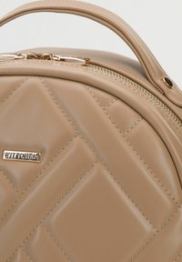 Beige quiltad handväska gjord av slät syntetisk läder, med ett handtag upptill och en guldfärgad dragkedja med varumärkeslogotyp.