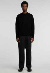 Schwarzer Strickpullover mit rundem Ausschnitt, kombiniert mit locker sitzenden schwarzen Hosen und schwarzen Schuhen. Glatte Textur, minimalistisches Design.