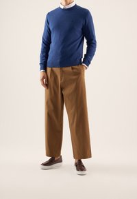 Modrý pletený svetr s kulatým výstřihem, hnědé široké kalhoty a tmavé slip-on boty. Stylové vrstvení s kontrastními barvami a texturami.