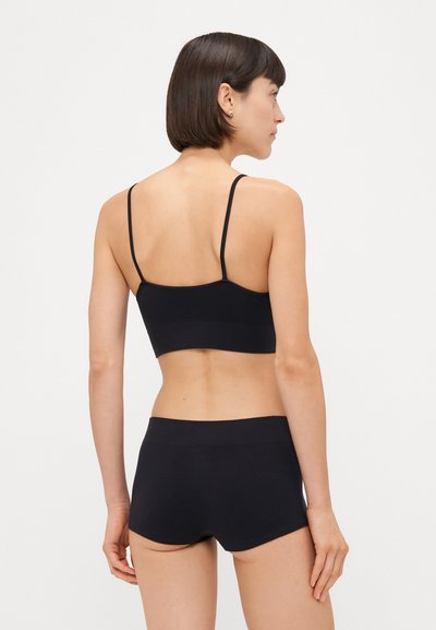 Čierny bralet s tenkými ramienkami, kombinovaný s čiernymi šortkami. Hladká textúra, minimalistický dizajn, bez ďalších ozdôb alebo vzorov.