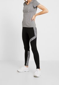 Camiseta gris de manga corta con el texto "CREW", combinada con leggings negros que presentan un patrón geométrico en blanco y negro texturizado en los laterales. Zapatillas blancas.
