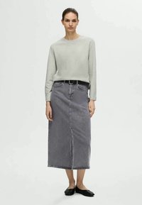 Top cinza de manga longa com tecido texturizado, combinado com uma saia midi de ganga de cintura alta em preto desbotado. Cinto preto e sapatos planos.