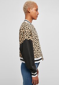  bomber jakna s uzorkom leoparda, crnim rukavima, prugastim kragnom i manžetama. Materijal ima glatku teksturu i ležeran kroj koji se završava iznad struka.