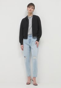 Haut à capuche noir court, t-shirt gris clair, jean bleu délavé déchiré et escarpins noirs à brides. Présente une coupe décontractée et un tissu texturé.