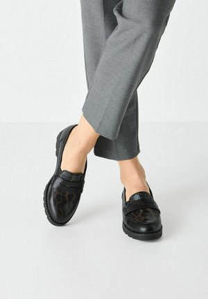 Black loafers featuring a leopard print panel, made of leather, with a smooth texture and rubber soles. Worn with gray, cropped pants.