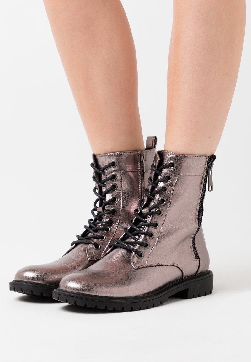 Botines metálicos en color rosa dorado con cordones en la parte delantera, cierre de cremallera lateral y suela de goma texturizada con tracción.