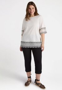 Witte top met zwarte kantdetails op de mouwen en zoom, gecombineerd met zwarte cropped broek en zwarte gemusterde espadrilles.