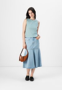 Lyseblå ärmeløs topp med dekorasjoner, kombinert med en utsvungen denimskjørt og en brun crossover-veske. Sorte loafers fullfører antrekket.
