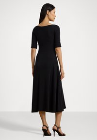 Black midi dress with short rolled sleeves, a wide neckline, and a flared hem. Worn with black high-heeled sandals. Smooth fabric texture.