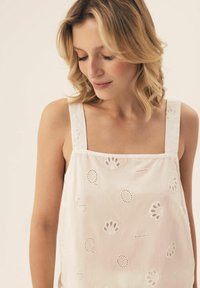 White, sleeveless top featuring embroidered patterns and cut-out details. Made from lightweight fabric, with square shoulder straps.