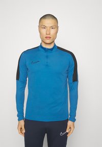 Nike majica dugih rukava u plavoj boji, sa zip ovratnikom, crnim naglascima na ramenima i prilagođenim dizajnom, izrađena od laganog materijala.