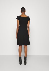 Svart kortärmad klänning med åtsittande överdel och utsvängd kjol, tillverkad av en slät tyg. Buren med svarta ankelboots och ett metallhalsband.