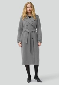 Cappotto lungo in misto lana grigio con bottoni doppi, cintura da annodare e tasche laterali. Presenta un colletto a scialle e maniche lunghe.