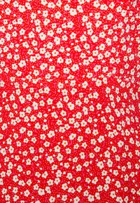 Tela roja brillante con un patrón de pequeñas flores blancas con centros amarillos y diminutos puntos blancos dispersos.