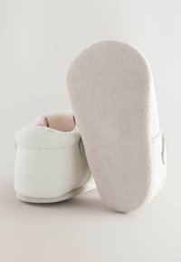 Chaussures pour bébé en cuir blanc avec des semelles en daim souple, arrière arrondi et doublure rose à motifs visible à l'intérieur. Accents de couture subtils.