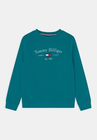 Tyrkisk sweatshirt med lange ærmer og ribbede manchetter. Indeholder "Tommy Hilfiger" logo i hvid, med et rektangulært flagemblem og "Est. 1985."