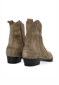 Un par de botas de ante en color topo, con cremalleras laterales, adornos de tachuelas en los bordes superiores y tacones bajos en negro.