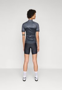 Fietsjersey in donkergrijze stof met een ademende meshstructuur. Voorzien van korte mouwen, een hoge kraag en een achterzak. Gekozen in combinatie met zwarte shorts.
