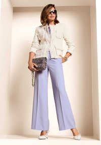 Witte tweedjas met gescheurde randen, licht lavendelkleurige wijde broek, gemusterde handtas en witte gehakte muiltjes met strikken. Zwarte zonnebril.