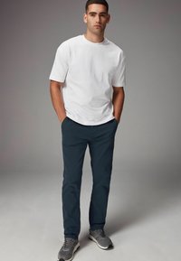 Camiseta de algodón blanca, de mangas cortas, corte relajado, combinada con pantalones chinos azul oscuro y zapatillas grises con acentos oscuros.