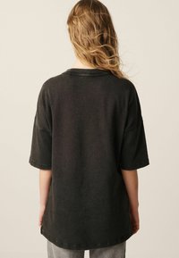 Black oversized t-shirt with a round neckline, short sleeves, and visible stitching details; fabric appears soft and textured.
