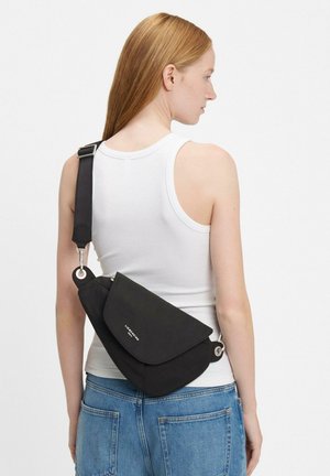 Czarna torba na ramię z klapką, srebrnymi elementami i regulowanym paskiem, noszona na krzyż. Prosty, minimalistyczny design.