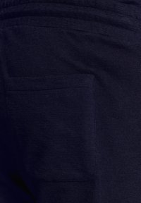 Marineblauwe stof met een gestructureerd oppervlak en een achterzak. Het materiaal lijkt zacht en licht rekbaar, ontworpen voor comfort.