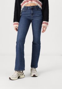 Uppklippta denimjeans i mörkblått, hög midja med en slät yta. Matchas med beige sneakers med mesh och gummikonturer.