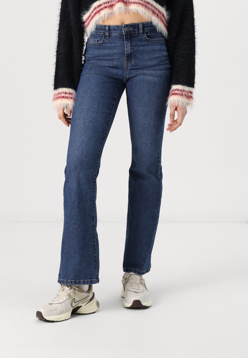 Uppklippta denimjeans i mörkblått, hög midja med en slät yta. Matchas med beige sneakers med mesh och gummikonturer.