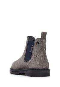 Botín de ante gris hasta el tobillo con paneles laterales elásticos y una etiqueta en la parte trasera, con un acabado texturizado y una suela de goma negra.