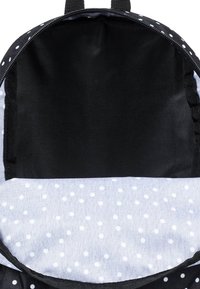 Öppen svart ryggsäck med vita prickar som visar en tom huvudfack och inre tygfoder med vita prickar.