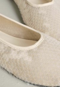 Bēša baleta dzīvokļzābaki ar teksturētu, caurspīdīgu tīklojuma augšdaļu, apaļu purngalu un vieglu spīdumu. Gluda iekšējā oderējuma un mīkstināta zolīte.