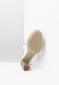 Sandale à talons hauts blanche avec une semelle texturée, dotée de fines brides et d'une semelle en caoutchouc beige. Fabriquée en Italie avec une semelle intérieure rembourrée.